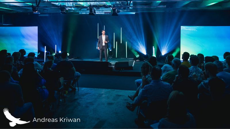 Andreas Kriwan auf einer großen Bühne vor Publikum im blauen Scheinwerferlicht